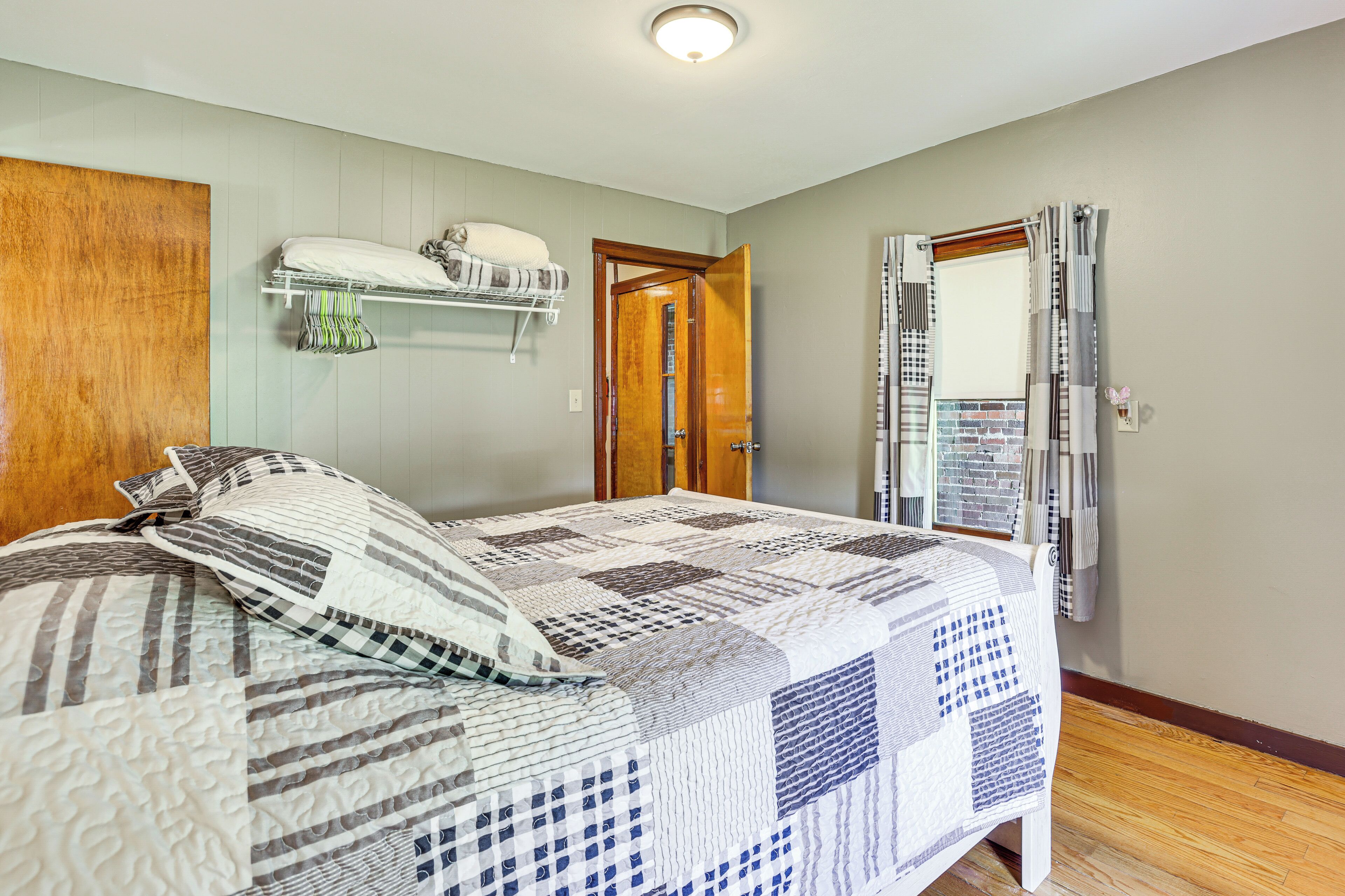 A bedroom with a bed, a wooden headboard, a closet with hanging clothes, and a door leading to another room.