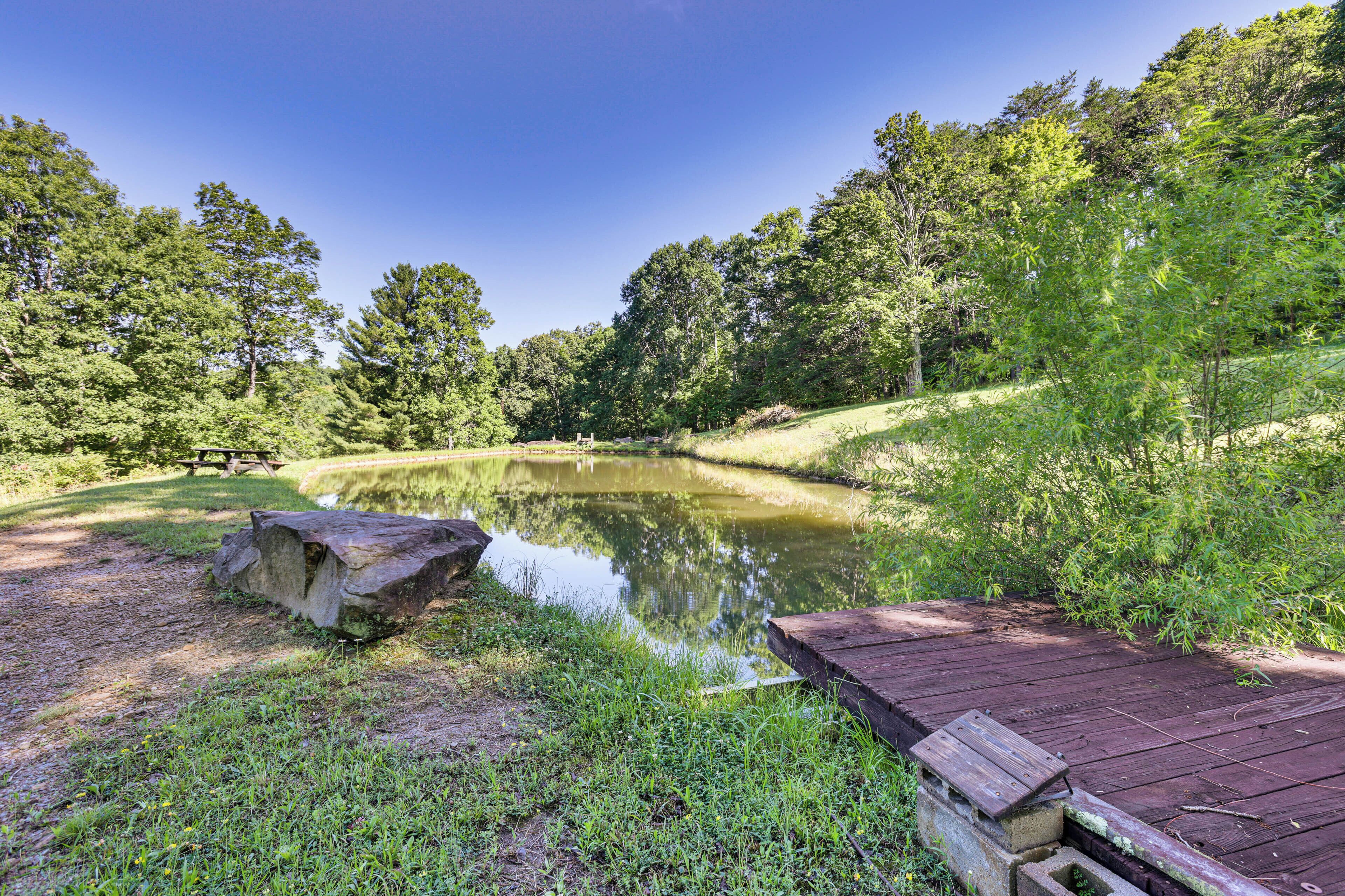 A serene pond surrounded by lush greenery, a wooden deck, and a picnic table.