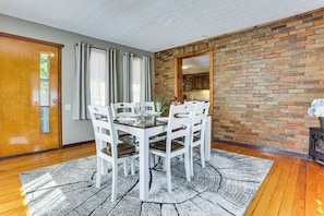 A dining area with a brick wall, wooden flooring, and a white dining set. - Game Room + Patio: Hilltop Home in Hocking County (Logan)