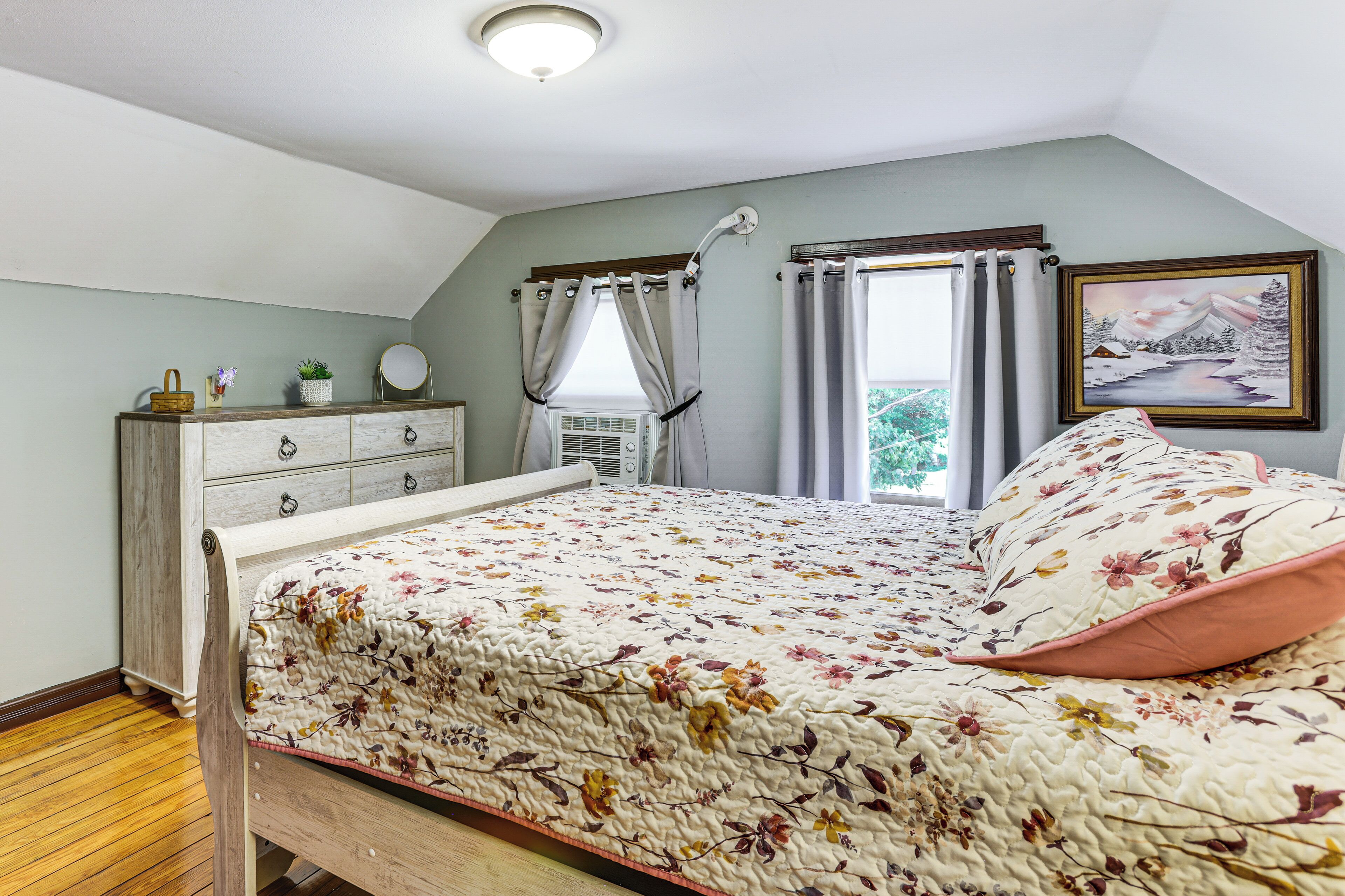 A bedroom with a bed, dresser, window with curtains, and a painting on the wall.