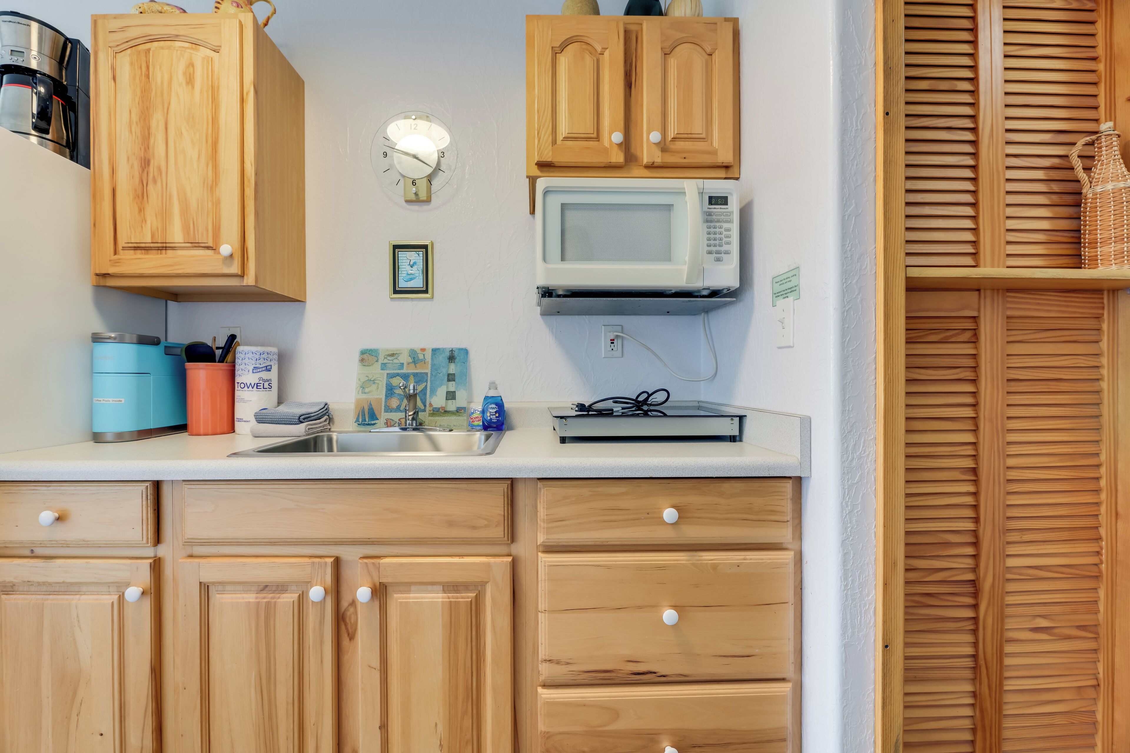 A kitchen with wooden cabinets, a microwave, a coffee maker, and a sink.