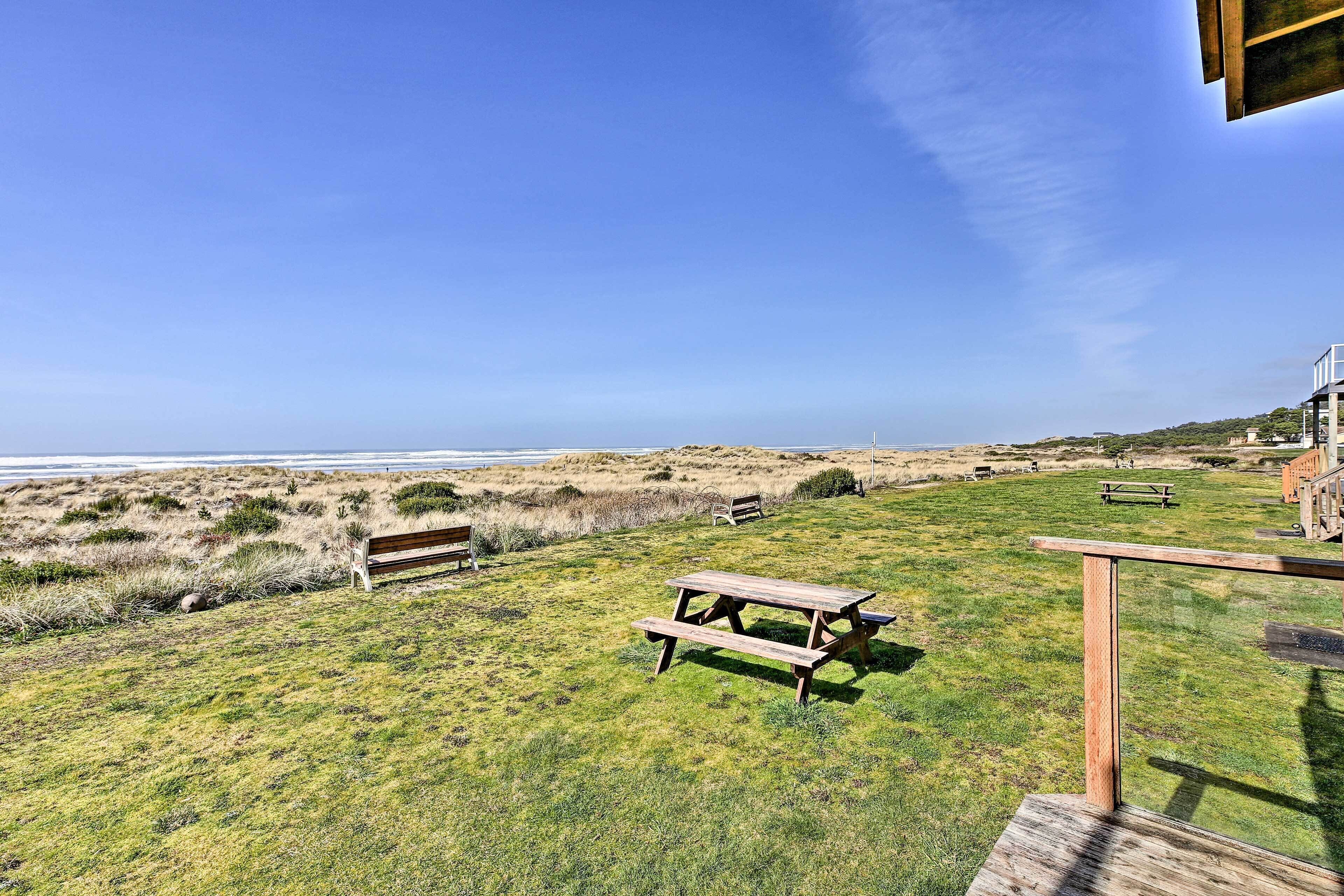 A grassy area with picnic tables and benches overlooking a beach.
