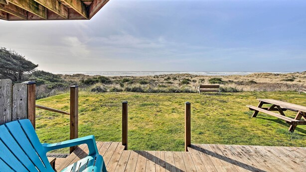 Une terrasse en bois avec une table de pique-nique et une chaise bleue, donnant sur une zone herbeuse bordée d’une clôture en bois et agrémentée d’un banc.