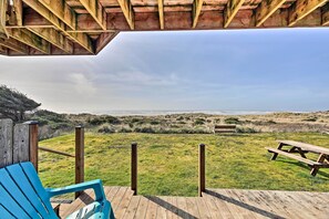 Una terraza de madera con una mesa de picnic y una silla azul, con vista a un área verde con una cerca de madera y un banco.
