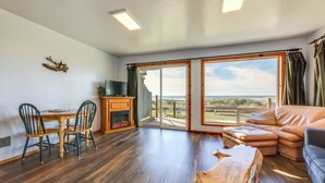 Un vaste espace de vie doté d’un plancher en bois, d’un canapé, d’une table basse et d’une table à manger avec des chaises. On y trouve également un téléviseur posé sur un meuble et une vue sur l’extérieur grâce à de grandes fenêtres.
