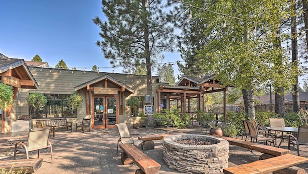 An outdoor patio area with wooden benches, a stone fire pit, and a building with a sign.