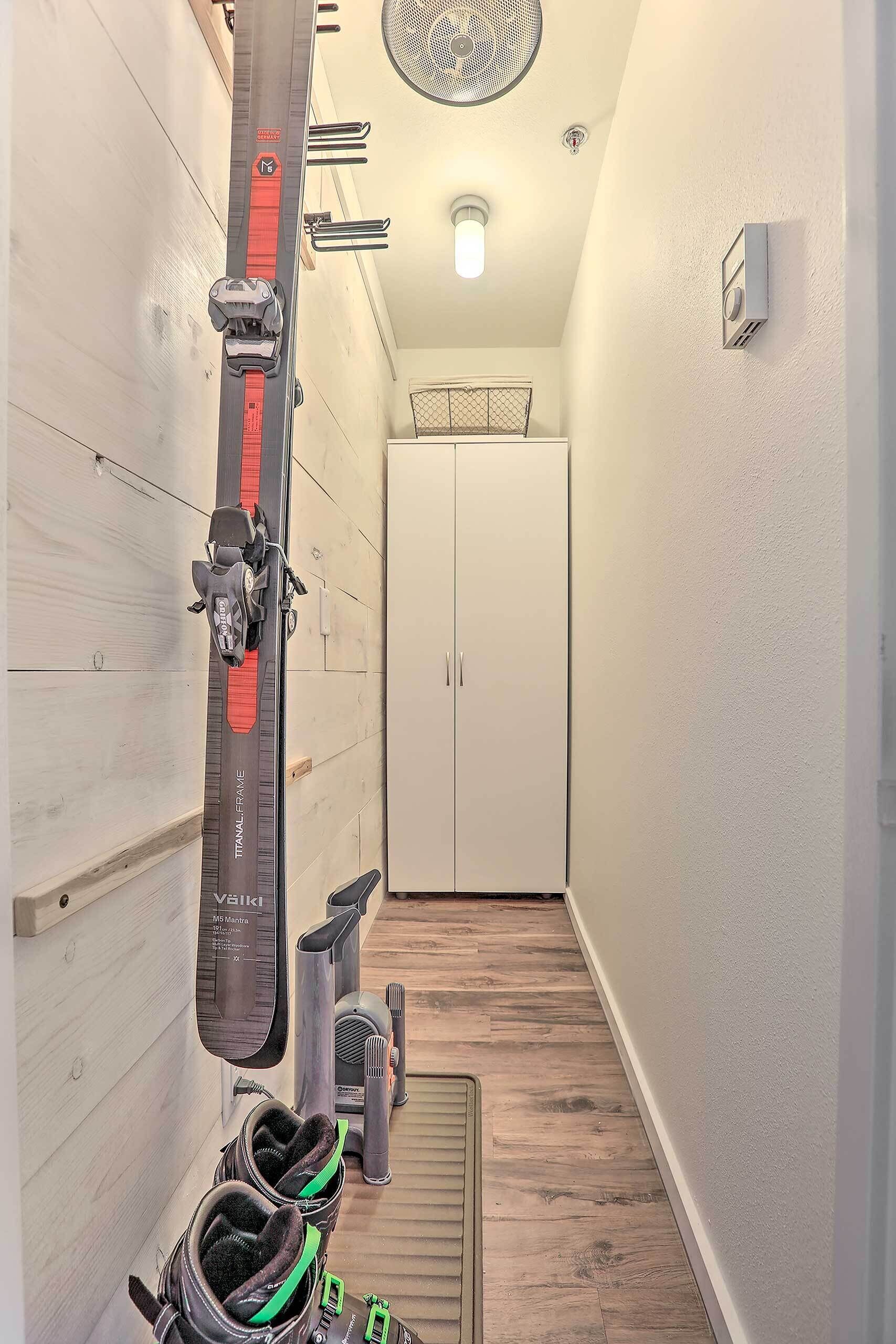 A narrow hallway with a ski rack, a pair of skis, and a pair of boots.