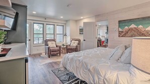 A modern bedroom with a large bed, two armchairs, a small table, and a painting on the wall.