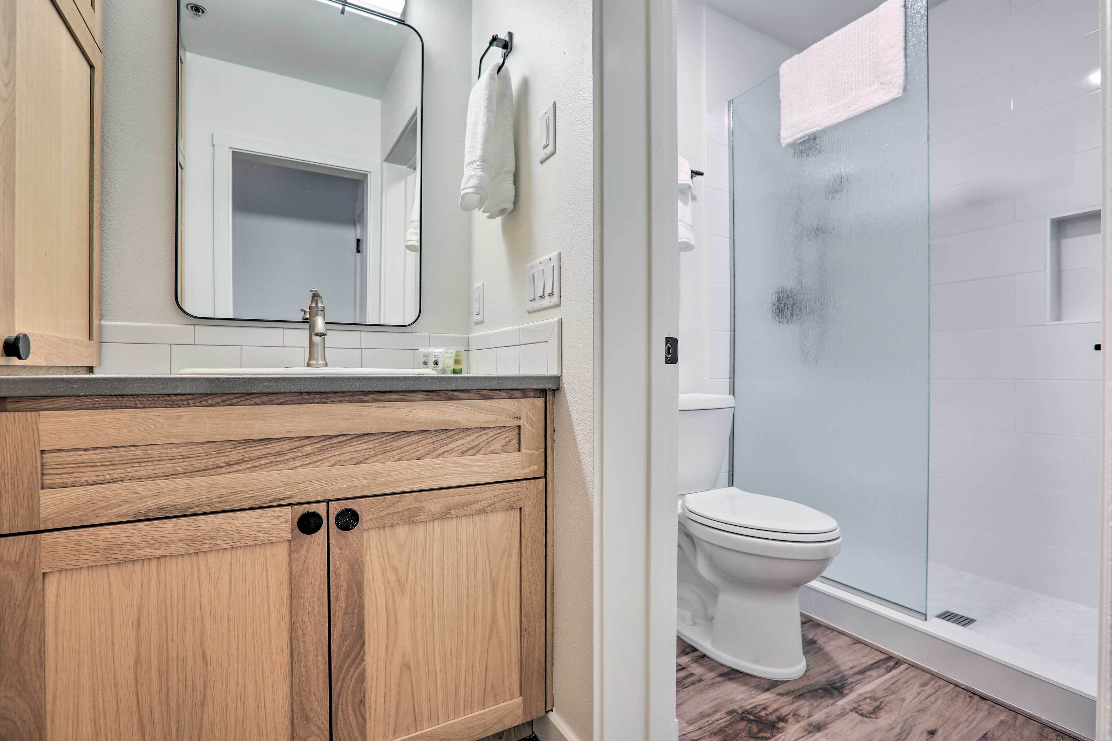 Une salle de bain avec un meuble-lavabo en bois, un miroir, des toilettes et une cabine de douche en verre.