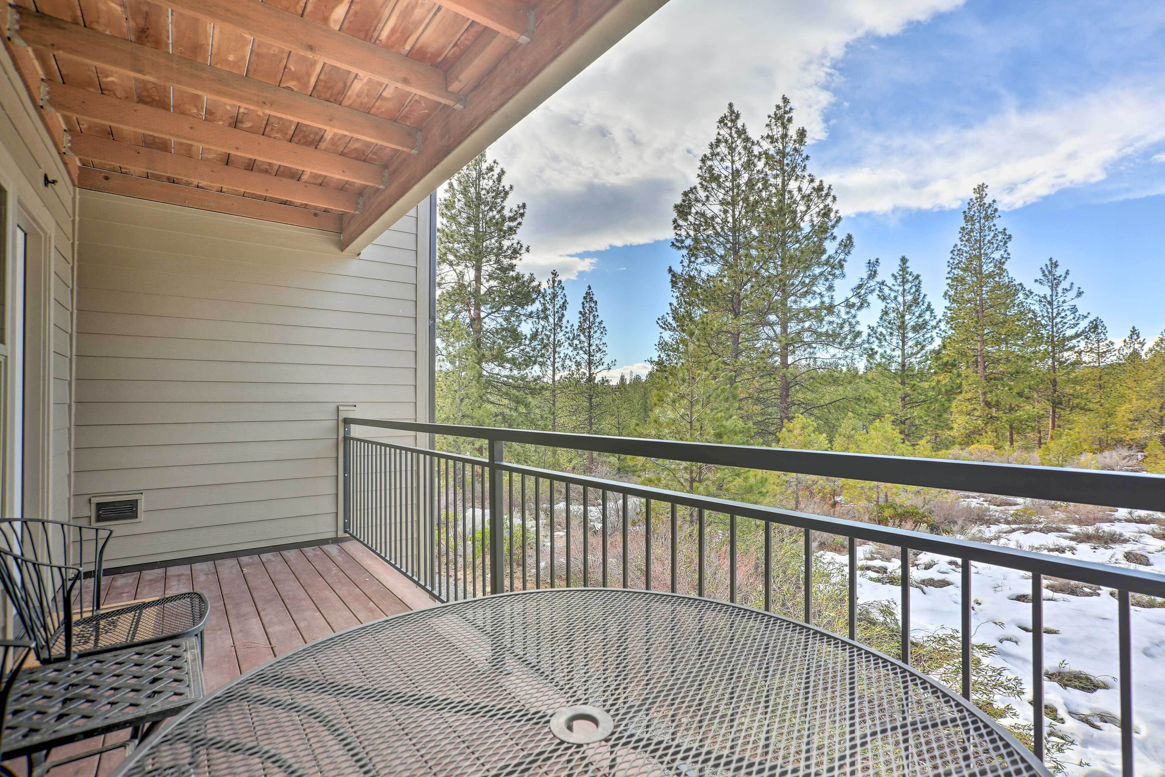 A covered outdoor area with a metal table and chairs, a wooden ceiling, and a view of a forested area with snow.