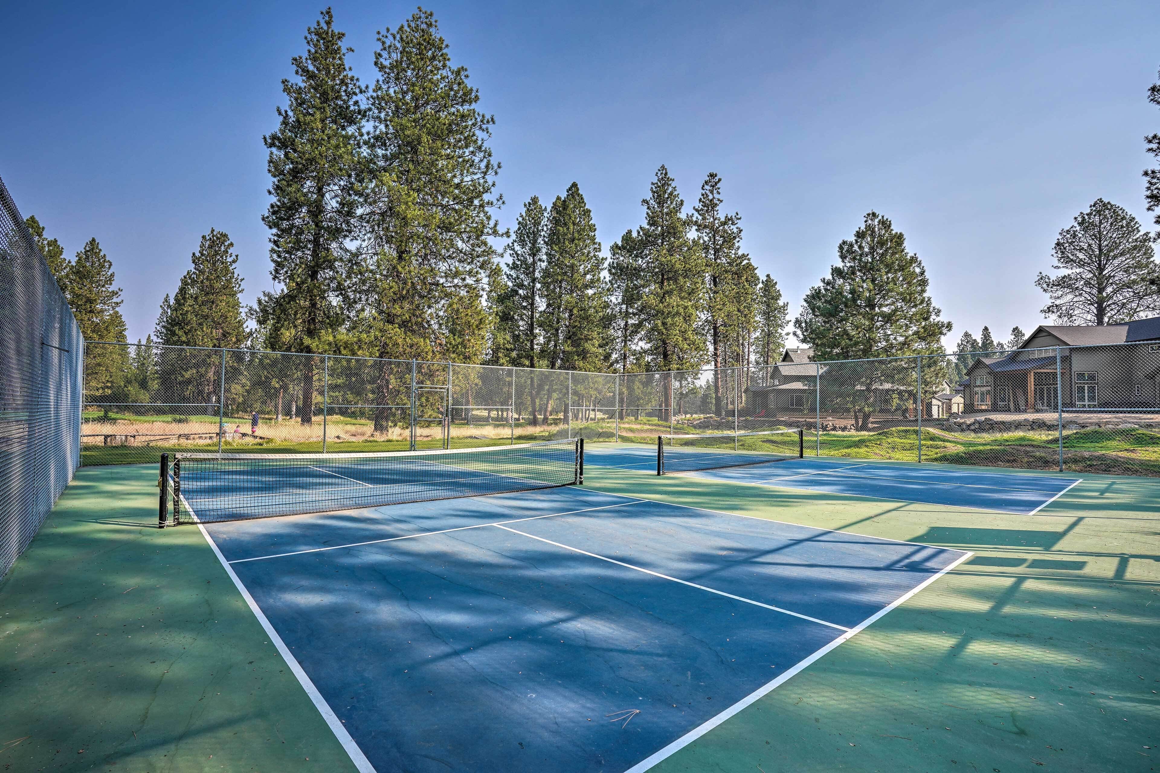 Cancha de tenis con red, rodeada de árboles y una valla.