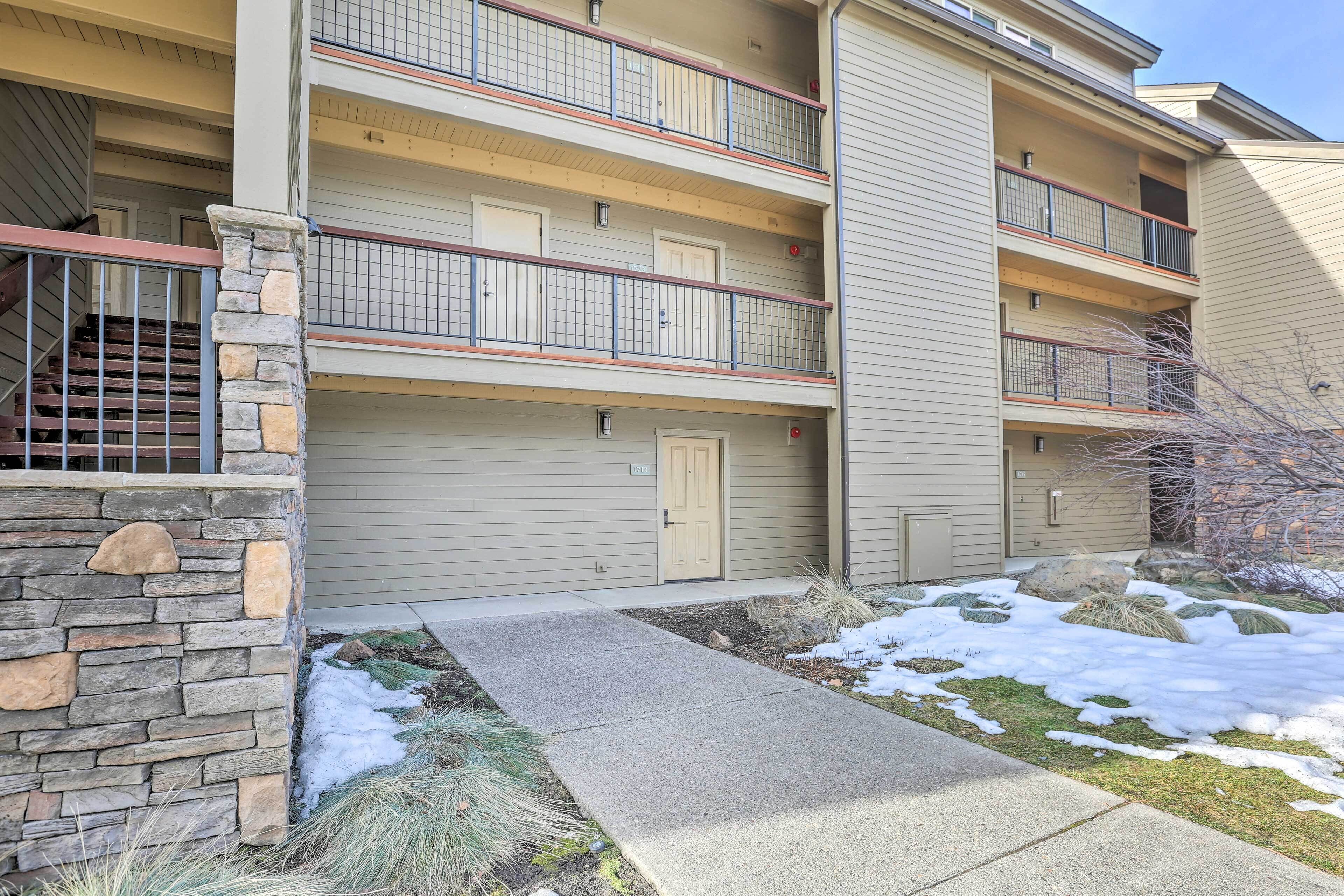 A multi-story residential building with balconies, a stone wall, and a snow-covered ground.