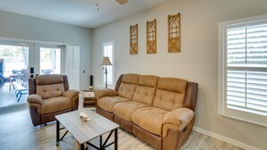 A living room with a brown leather sofa, a brown leather armchair, and a wooden coffee table. There is a ceiling fan, a window with blinds, and a door leading to an outdoor area. - Renovated Sunny Port St Lucie Home w/ Outdoor Pool (Port Saint Lucie)