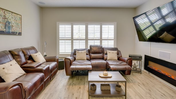 A living room with two leather sofas, a coffee table, a flat-screen TV, and a fireplace. - Renovated Sunny Port St Lucie Home w/ Outdoor Pool (Port Saint Lucie)
