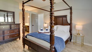 A four-poster bed with a wooden frame, a bedside table with a lamp, and a dresser with drawers. - Renovated Sunny Port St Lucie Home w/ Outdoor Pool (Port Saint Lucie)