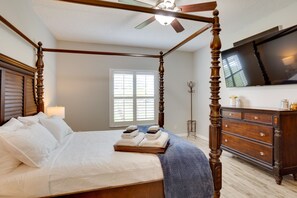 A four-poster bed with a wooden headboard, a bedside table with a lamp, and a dresser with a flat-screen TV. - Renovated Sunny Port St Lucie Home w/ Outdoor Pool (Port Saint Lucie)