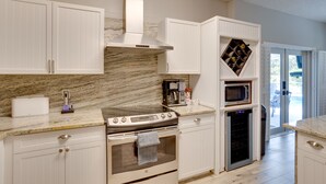 A modern kitchen with white cabinetry, a stainless steel range hood, a built-in oven, a microwave, and a wine rack. - Renovated Sunny Port St Lucie Home w/ Outdoor Pool (Port Saint Lucie)