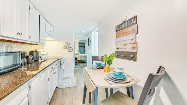 A modern kitchen with white cabinets, a granite countertop, and a dining area with a table set for two. - Walk to Downtown Albany: Ten Broeck Triangle Apt! (Albany)