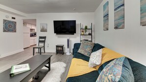 A modern living room with a flat-screen TV, a sofa with patterned cushions, a coffee table, and a small side table. - Walk to Downtown Albany: Ten Broeck Triangle Apt! (Albany)