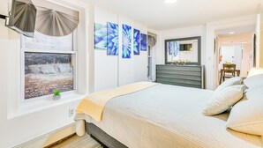 A bedroom with a bed, a window with curtains, a wall-mounted artwork, and a bedside table. - Walk to Downtown Albany: Ten Broeck Triangle Apt! (Albany)