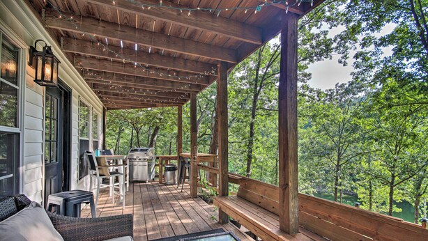 A covered outdoor deck with wooden furniture, a glass-top table, and a view of a forested area. - Private Fishing Dock: Grand Lake Home (Eucha)