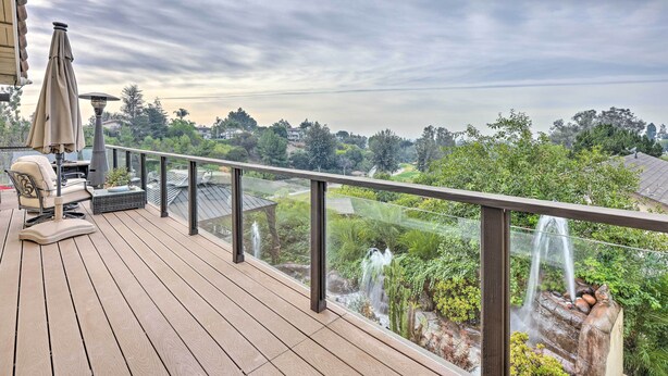 Een houten terras met tuinmeubilair, een glazen balustrade en uitzicht op een tuin met een waterval.