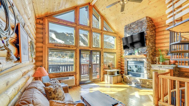 A log cabin interior with a stone fireplace, large windows, and a cozy seating area. - Cozy Mountain Condo Across From Snow King Ski Mtn! (Jackson)