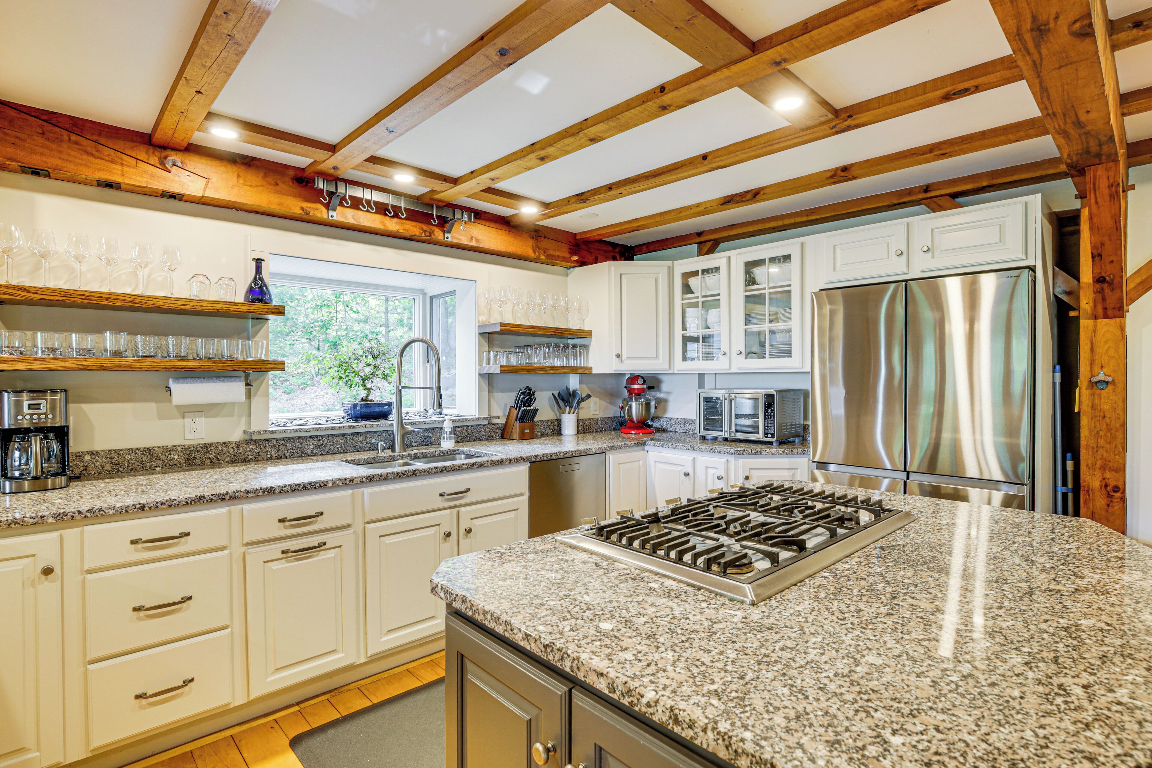 A kitchen with granite countertops, white cabinetry, stainless steel appliances, and wooden beams on the ceiling.