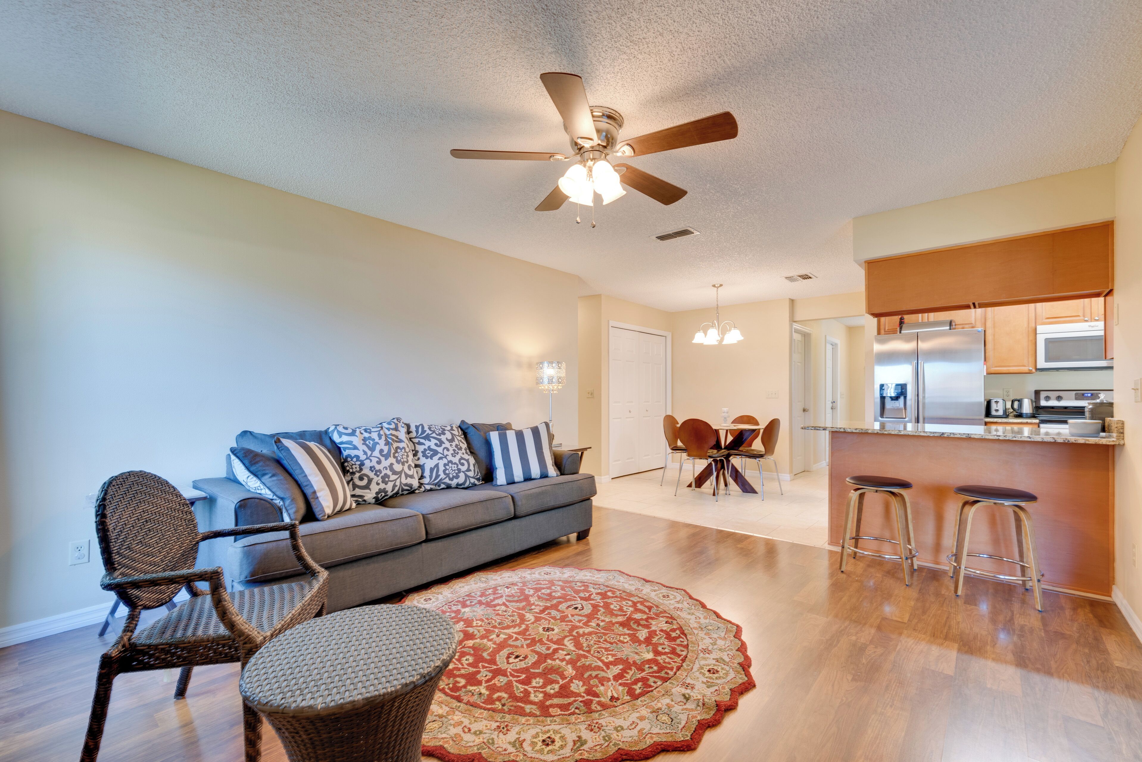 A modern living room with a sofa, chairs, a dining table, and a kitchen area with a refrigerator and microwave.