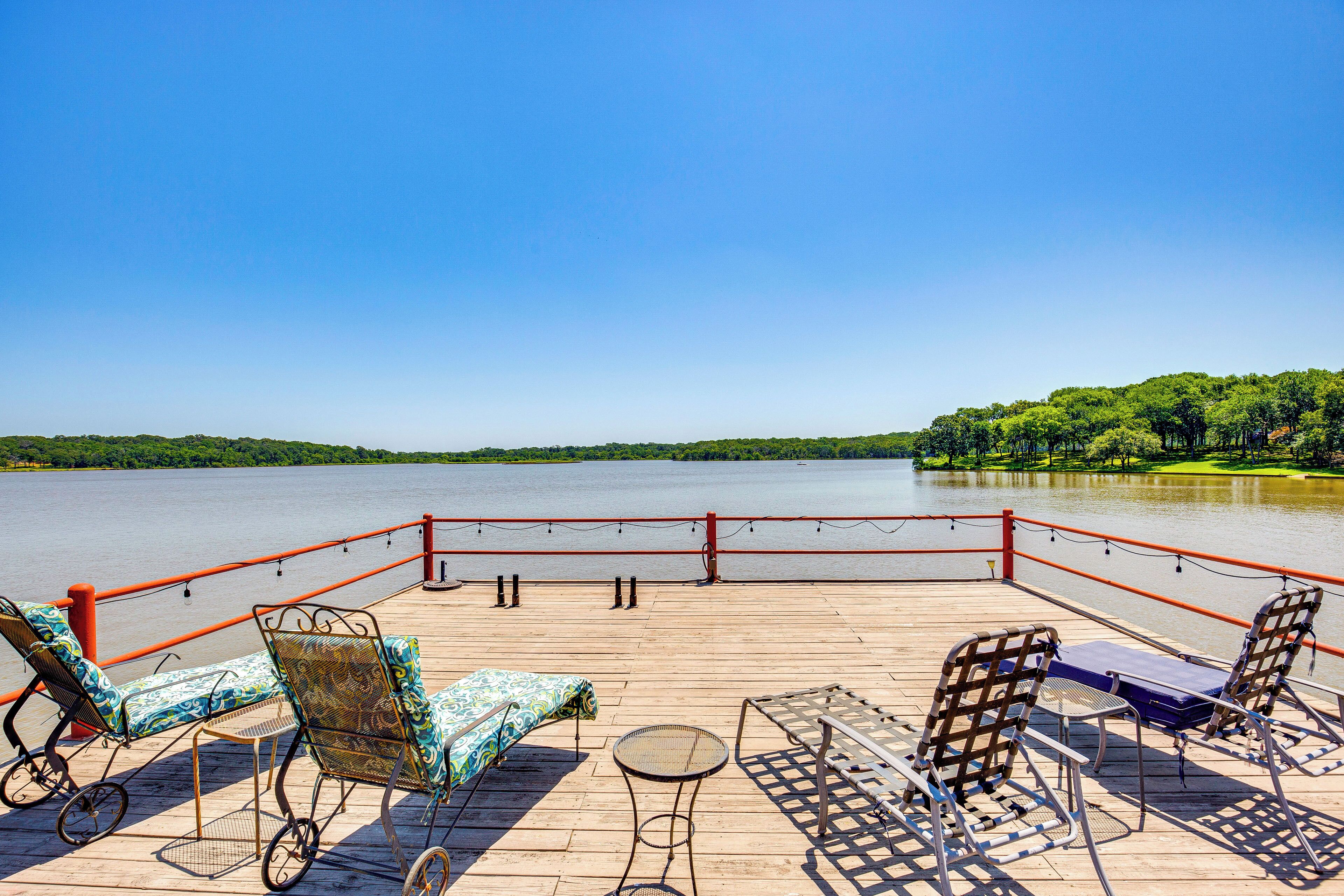 A wooden deck with lounge chairs and a table overlooking a calm lake, surrounded by a red railing.