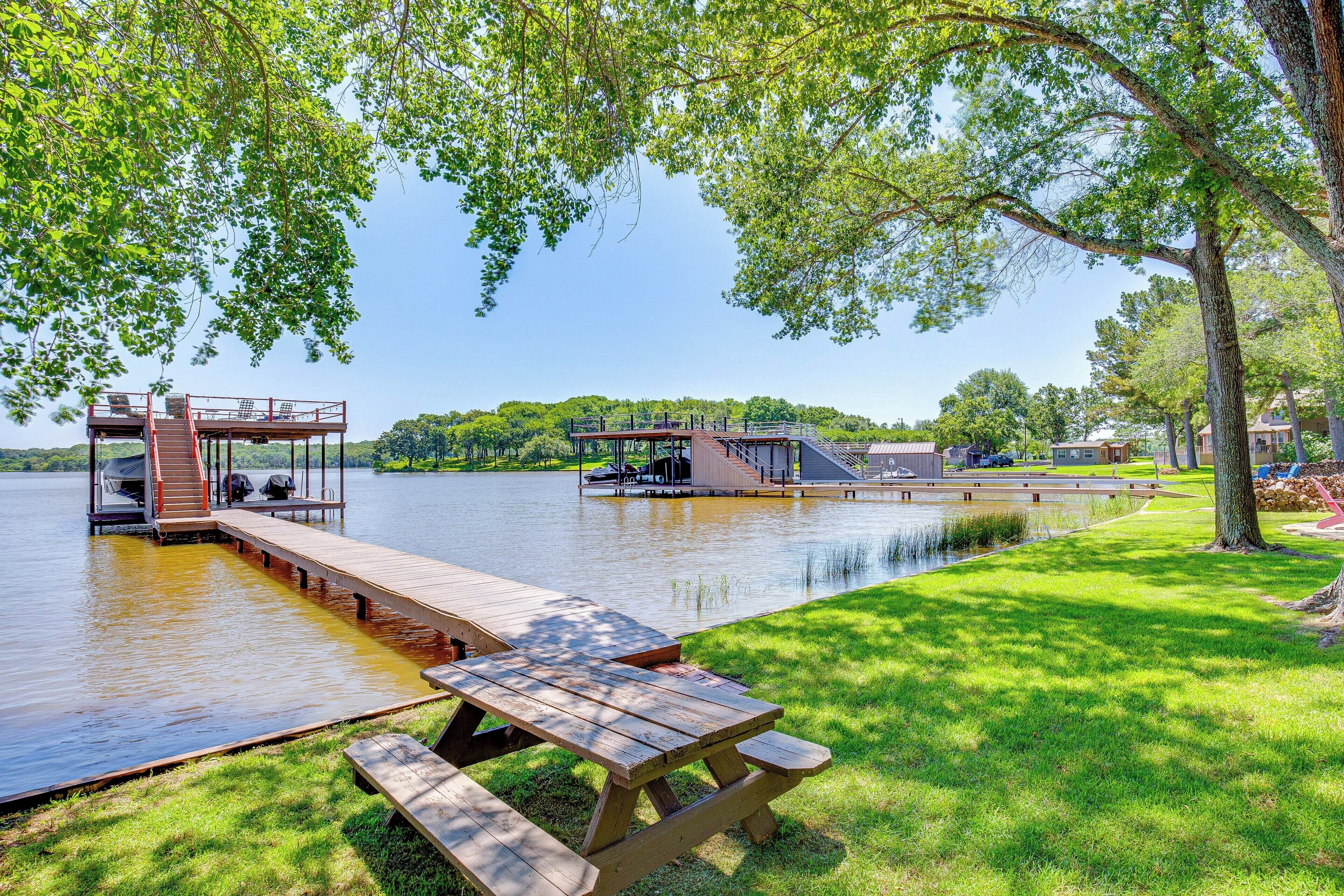 A lakeside park with picnic tables, a dock, and a covered area with stairs leading to a platform.