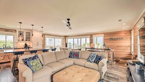 Uma sala de estar ampla com um sofá seccional bege grande, um banquinho estofado e uma parede de destaque em madeira com a inscrição "THE SAND BAR".
