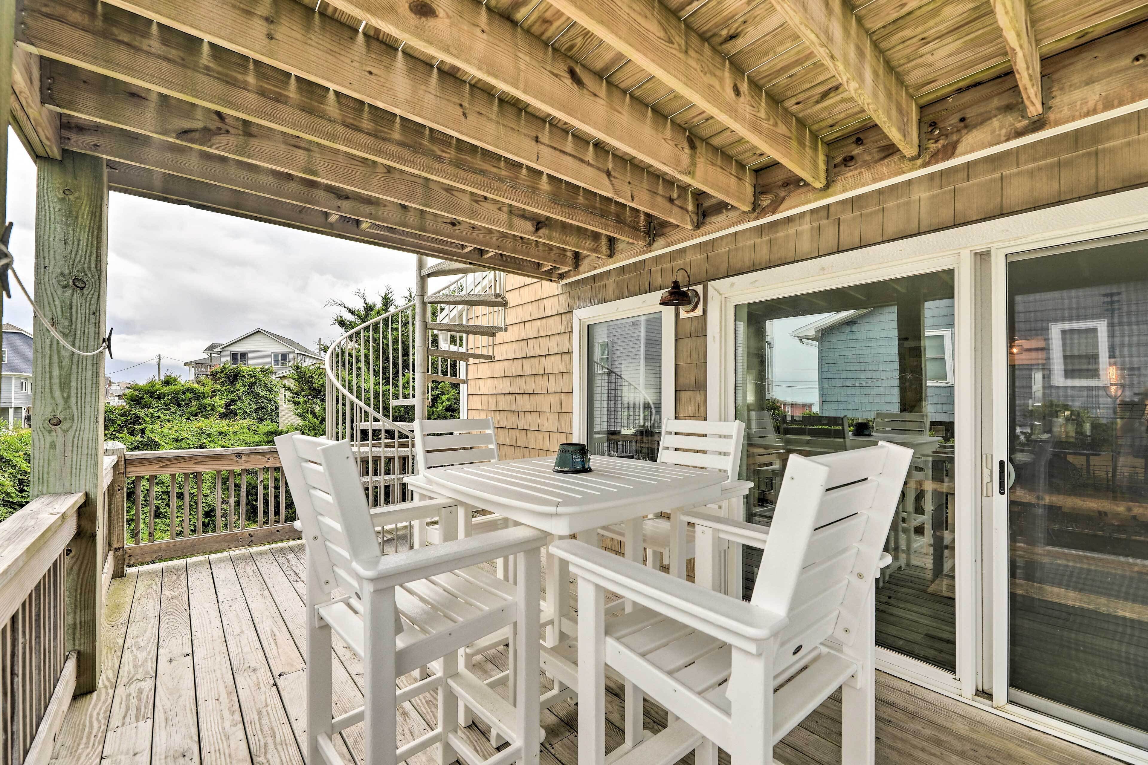 A covered outdoor area with a wooden deck, white chairs, and a table.