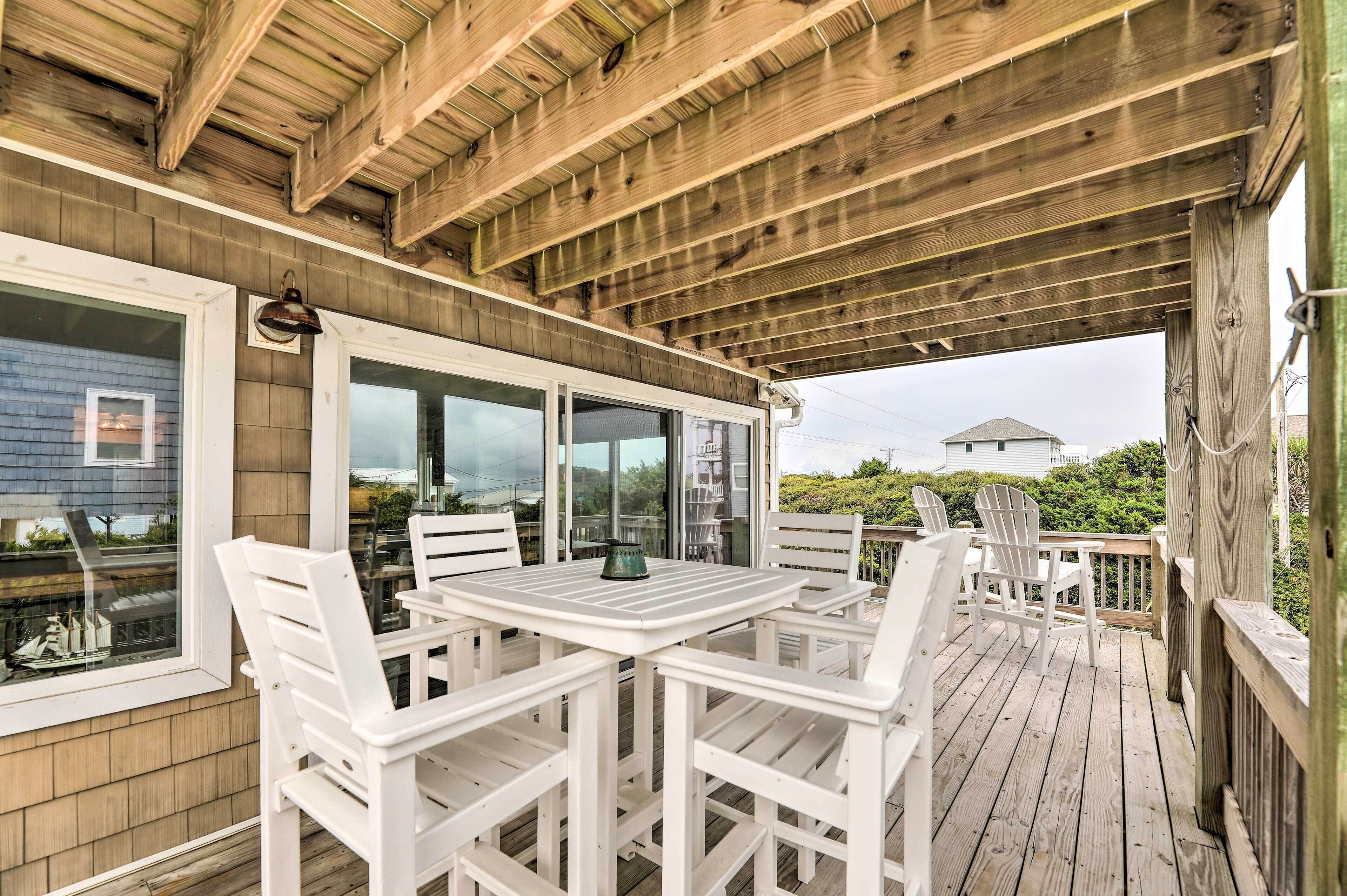 A covered outdoor deck with a wooden ceiling, white chairs, and a table.