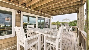 Um terraço coberto ao ar livre com teto de madeira, cadeiras brancas e uma mesa.