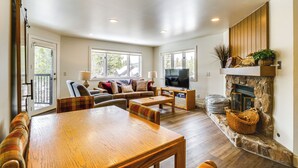 A spacious living room with a wooden dining table, a sofa set, a television, and a stone fireplace. - Hot Tub Access: Bright Breckenridge Condo (Breckenridge)