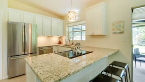 A kitchen with white cabinets, a stainless steel refrigerator, a granite countertop, a kettle, and a hanging light fixture. - 'uncle Louie's' Gulf Coast Gem w/ Outdoor Oasis (Bradenton)