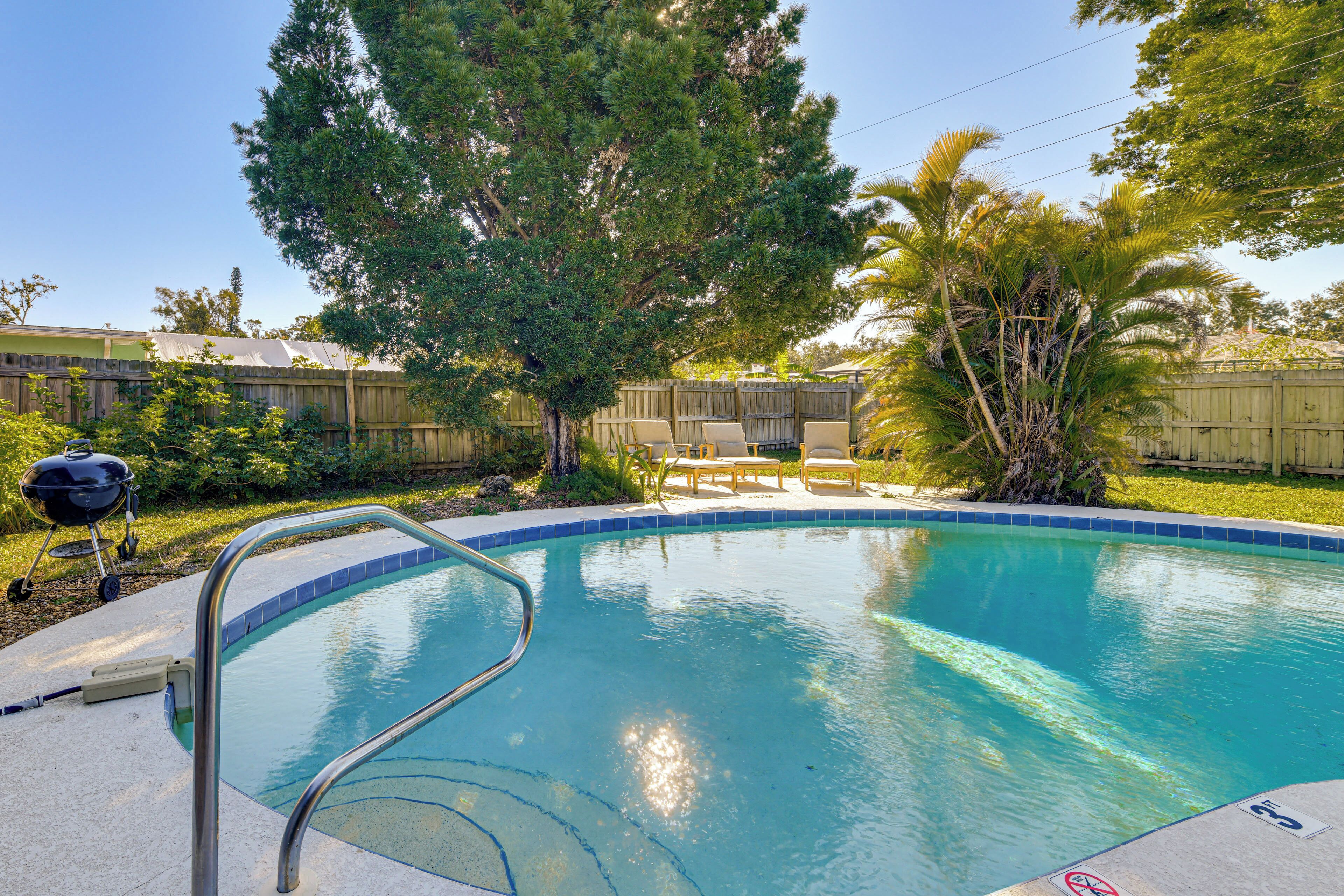 A backyard with a swimming pool, a wooden fence, and a barbecue grill.