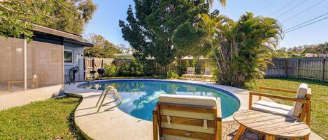 A backyard with a swimming pool, wooden deck, and outdoor furniture.