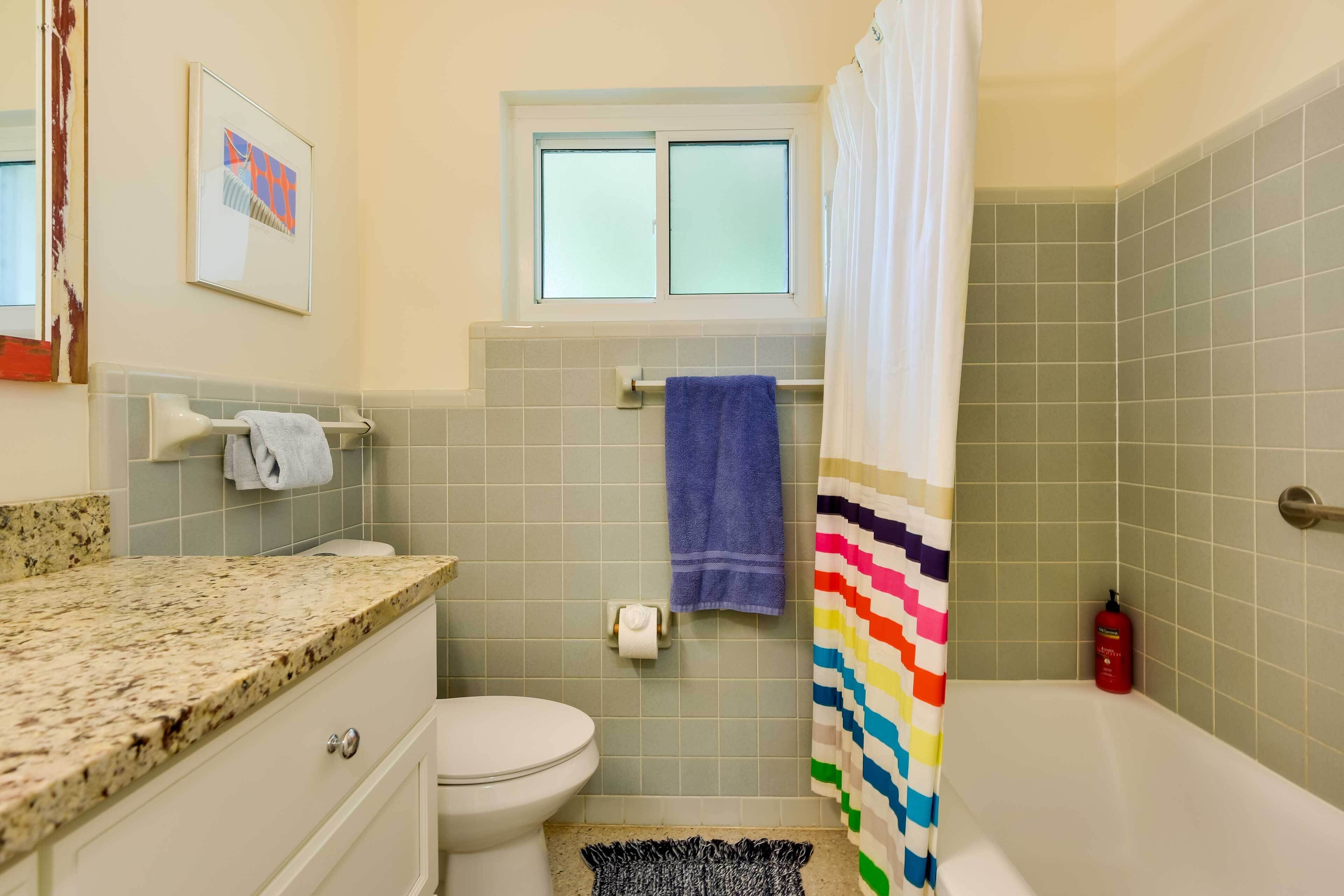 Ein Badezimmer mit Toilette, Waschbecken und Badewanne. Über der Toilette befindet sich ein Fenster, eine Handtuchstange und eine Duschvorhang.