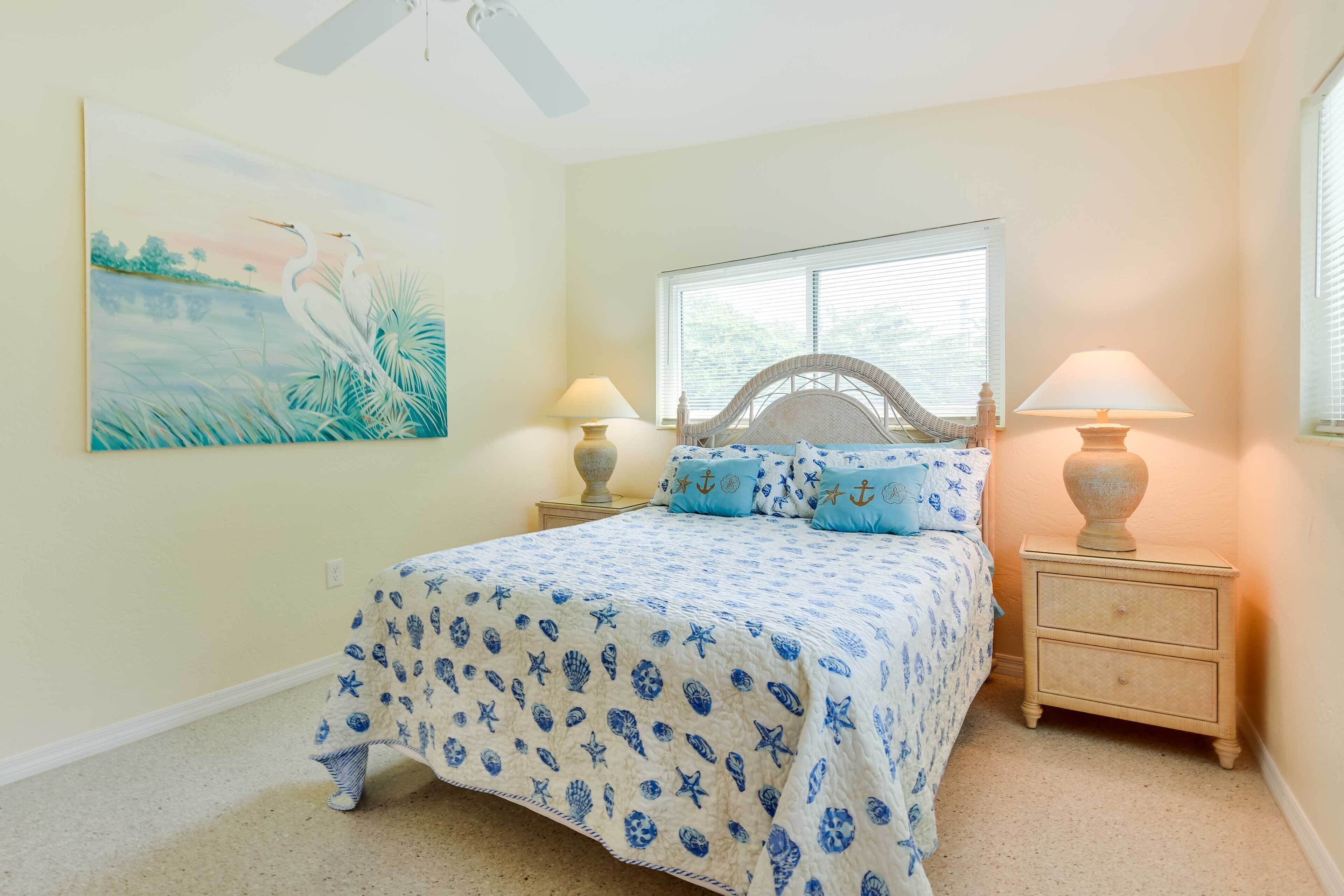 A bedroom with a bed, two nightstands, two lamps, a window, and a wall painting.