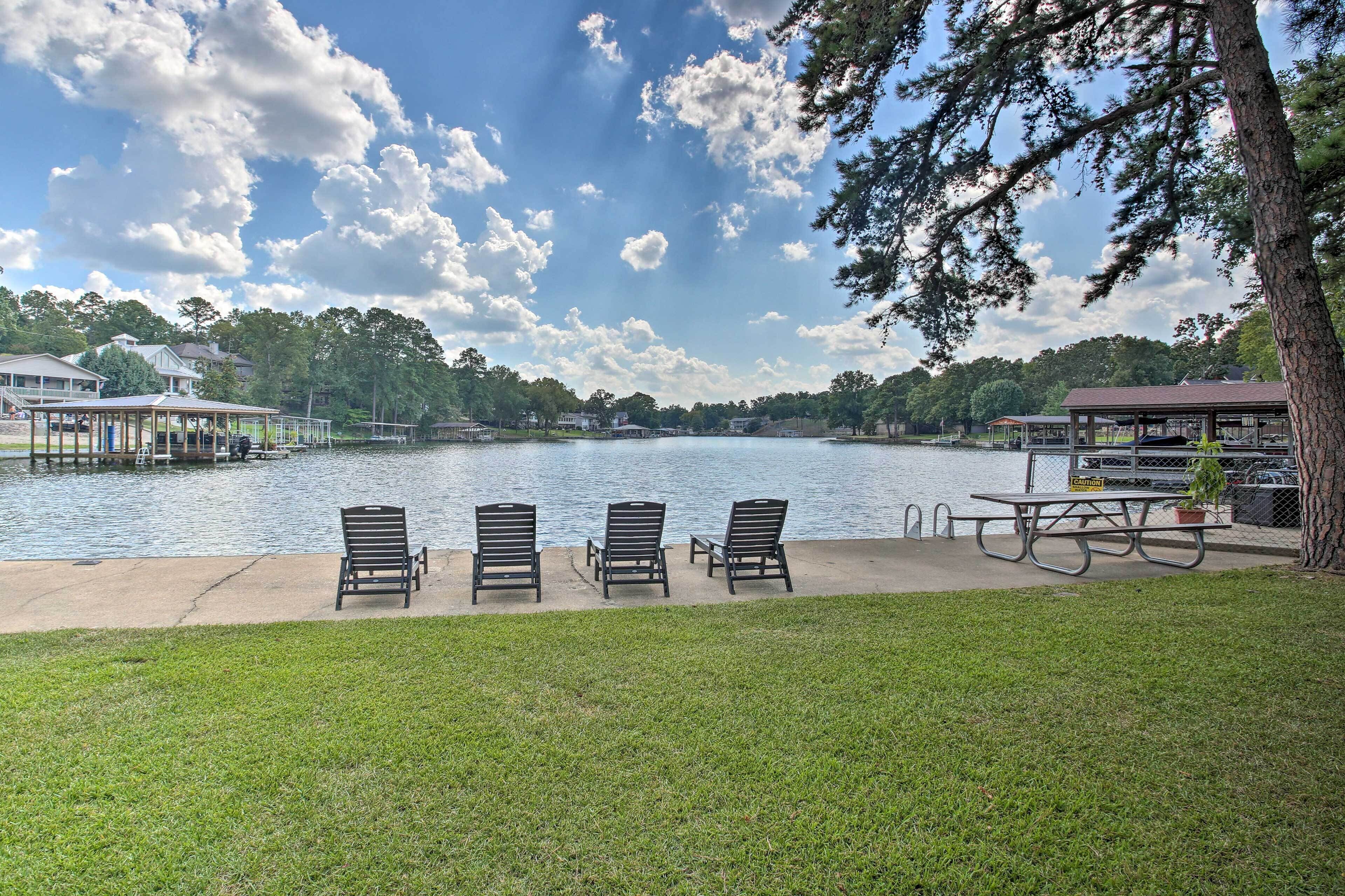 A lakeside patio with three lounge chairs, a picnic table, and a potted plant.