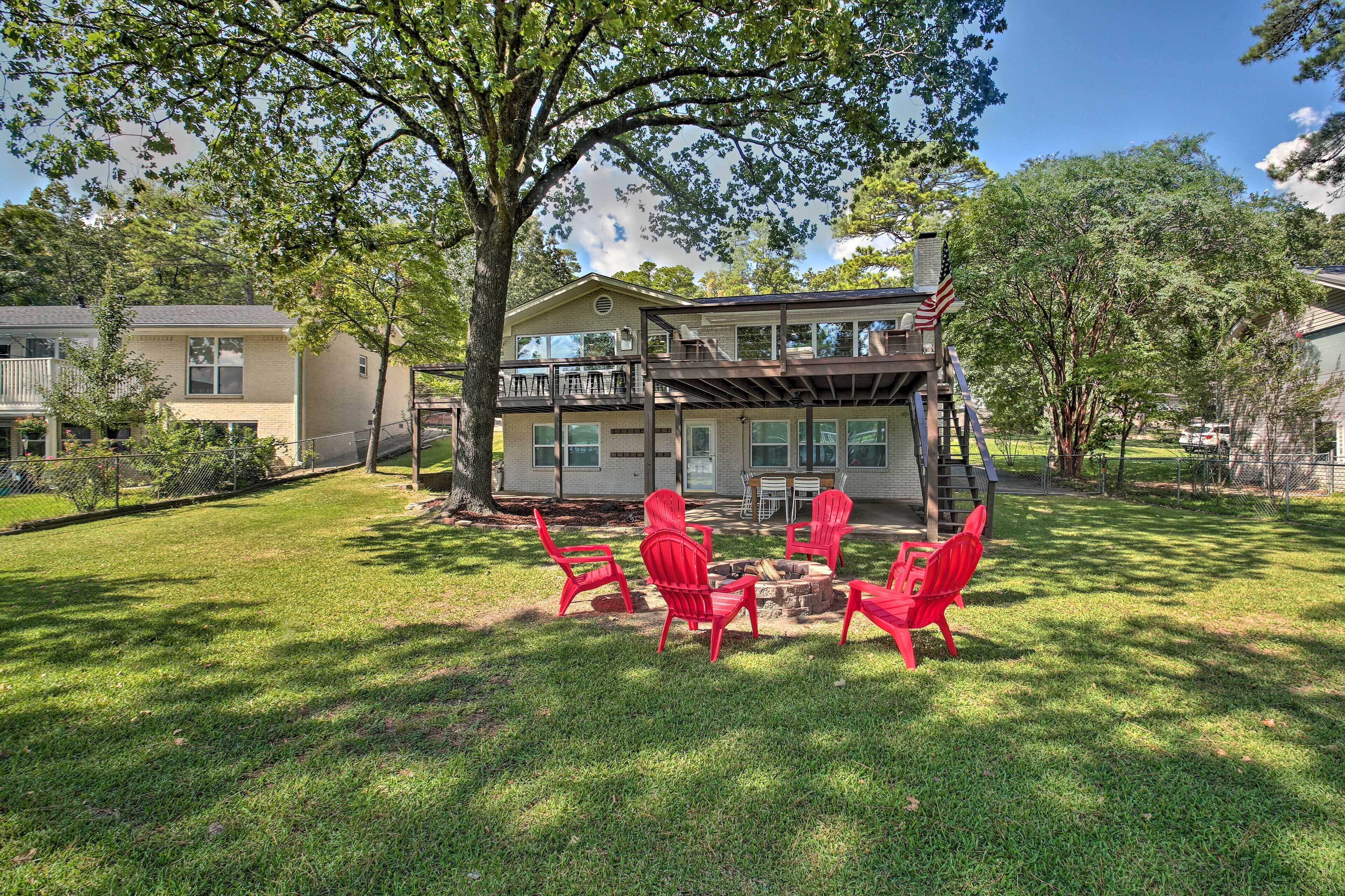 A two-story house with a deck, a fire pit, and red chairs in the yard.