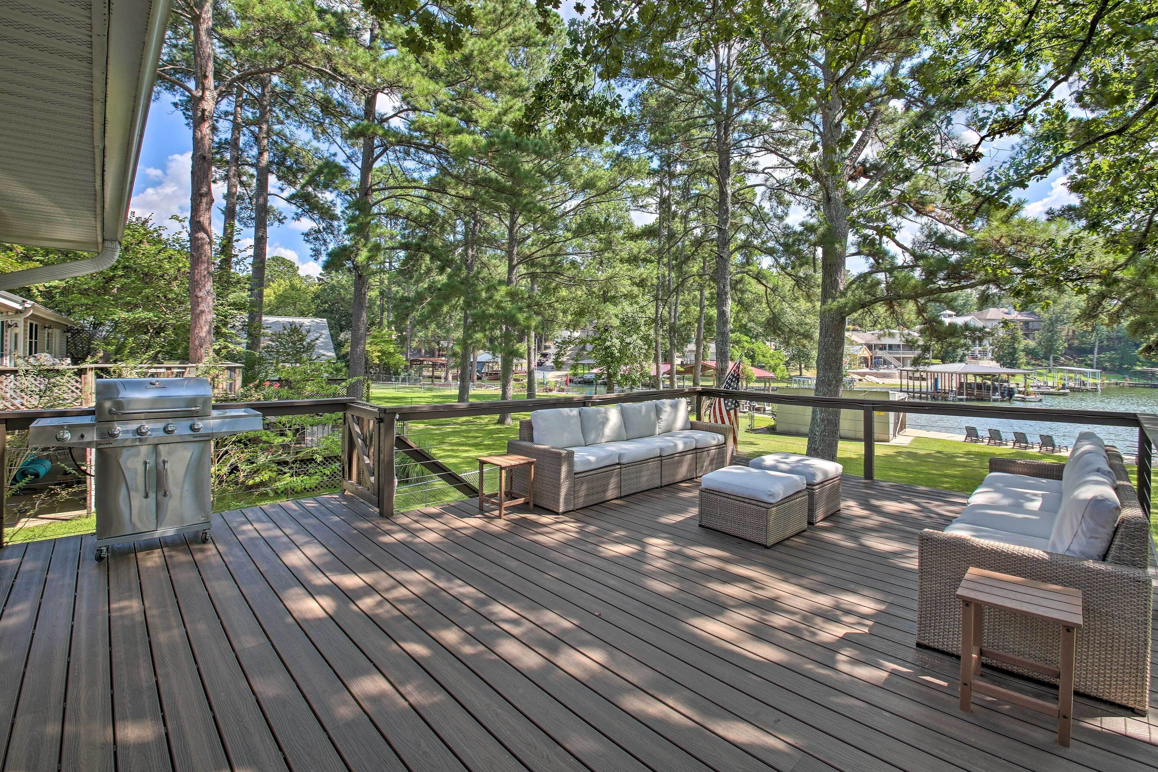 Una terraza de madera con mobiliario exterior, una parrilla y vistas a un lago.