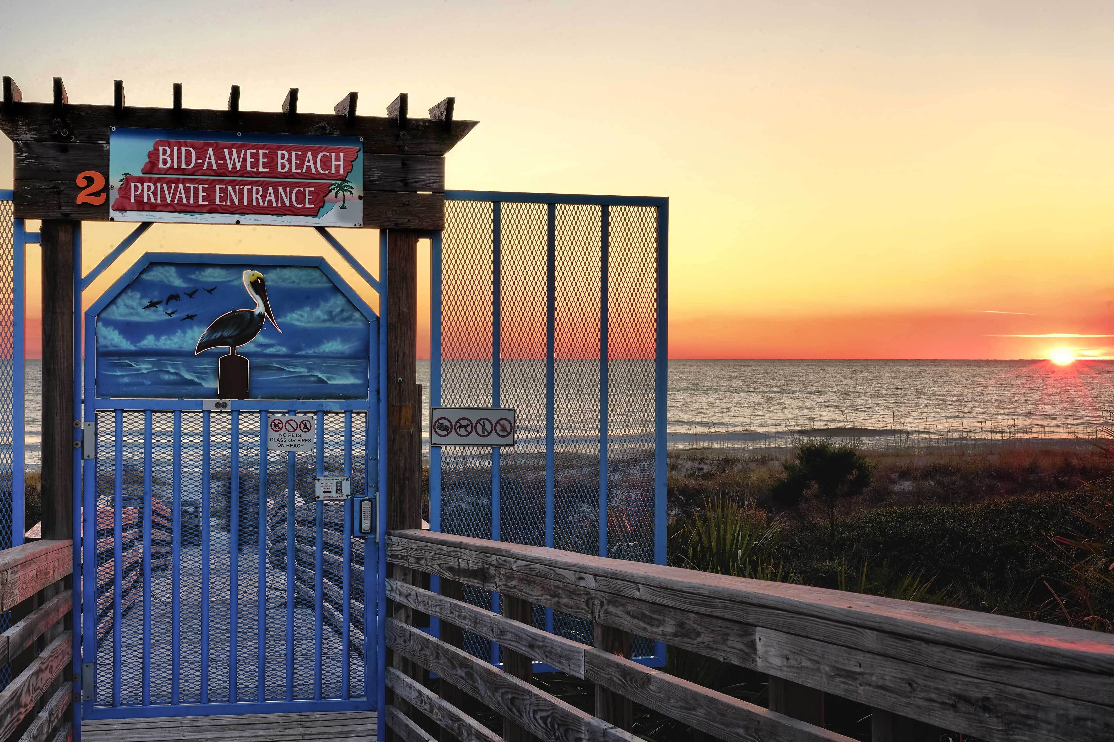A private entrance gate to Bid-A-Wee Beach with a wooden deck and a sunset view.