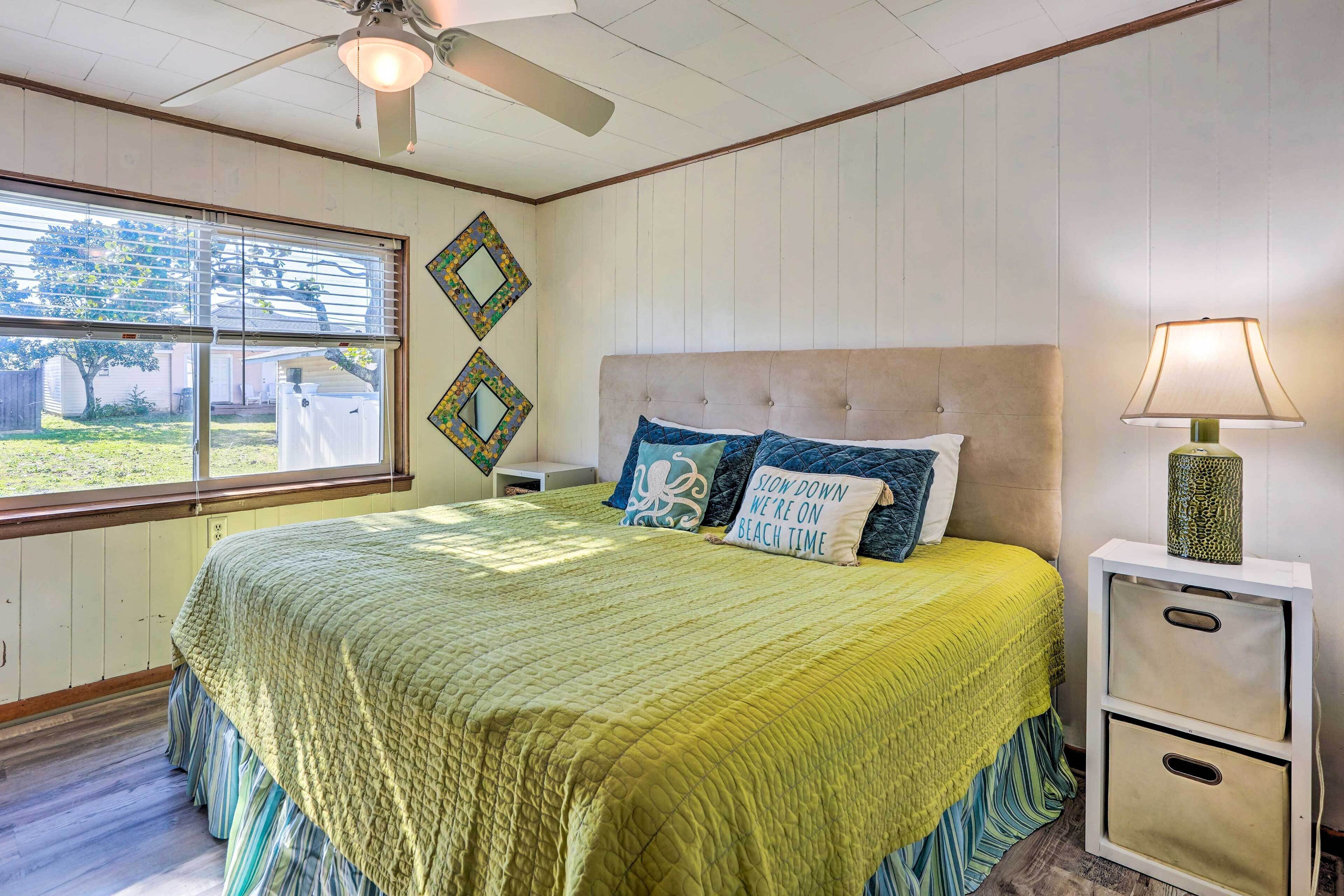 A bedroom with a large bed, a nightstand with a lamp, and a window with blinds.