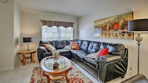 A living room with a black leather sofa, a glass coffee table, a lamp, and a painting on the wall. - Saltwater Pool, Spa & Lanai: Bradenton Home (Bradenton)