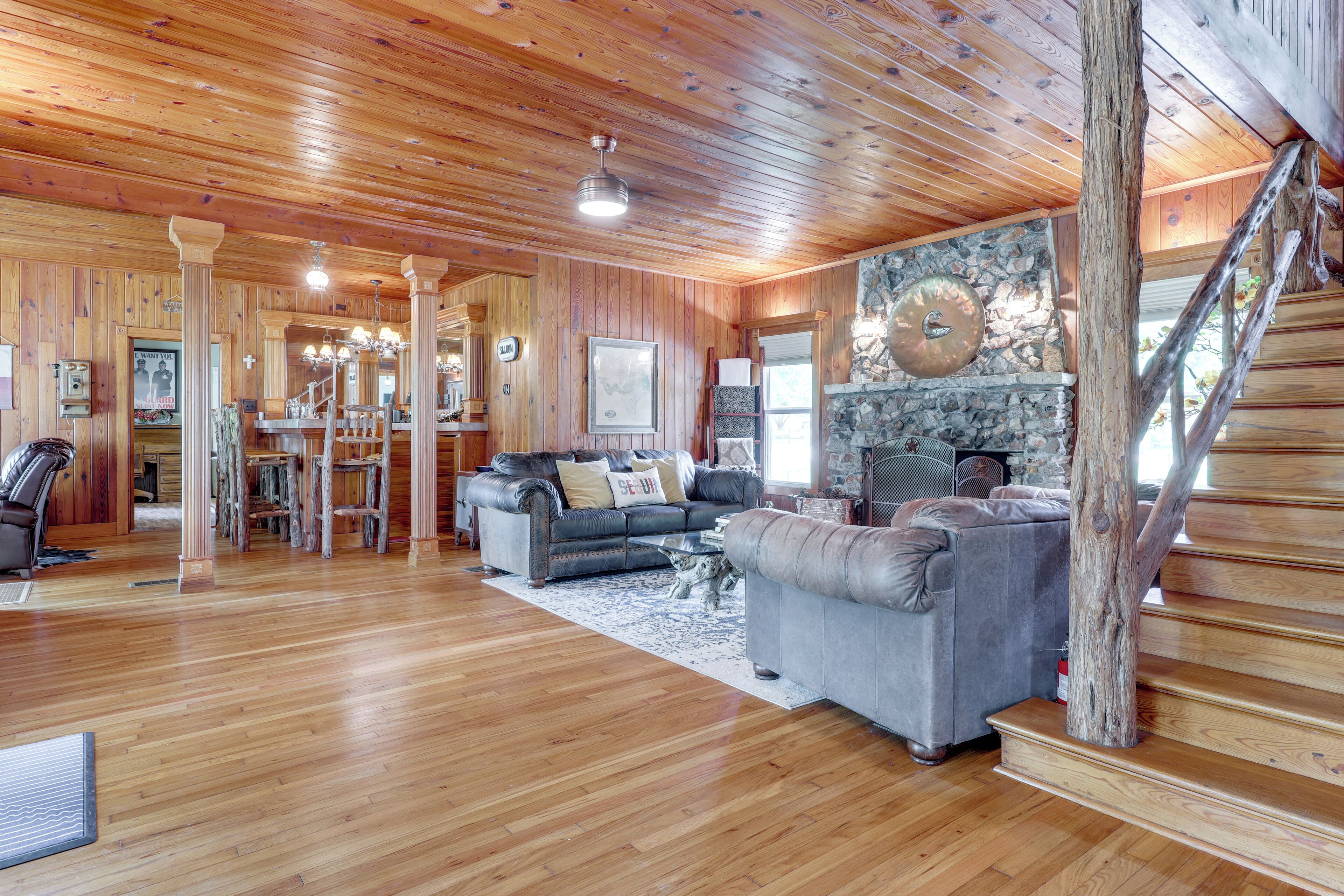 A spacious living room with wooden flooring, a grey sofa, a dining area with a stone wall, and a staircase.
