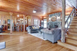 A spacious living room with wooden flooring, a grey sofa, a dining area with a stone wall, and a staircase. - Spacious Lake Placid Retreat w/ Gorgeous Views! (Seguin)