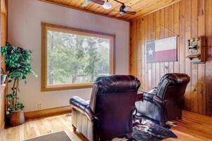 Quarto com paredes de madeira, uma janela grande, duas poltronas de couro, uma bandeira do Texas e um cofre fixado na parede.